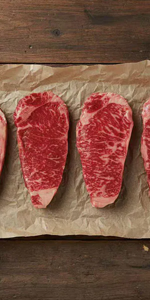 Raw marbled wagyu steaks on brown paper over wood at Hibachi Catering 4 U, a Chinese restaurant in Anselmo